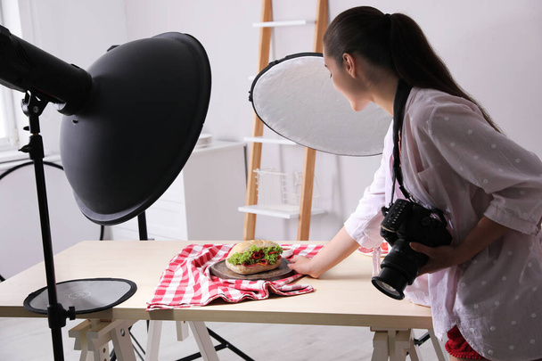 Young woman creating composition with sandwich in studio. Food photography - Фото, изображение