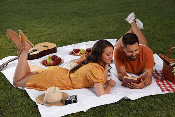 Happy young couple reading book on picnic plaid outdoors - Foto, imagen