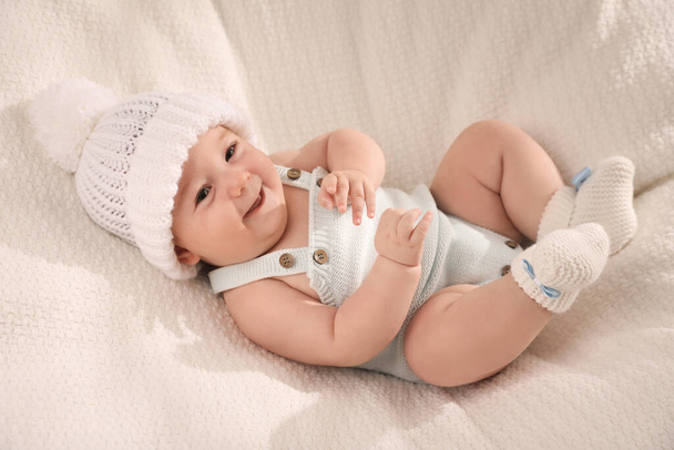 Χαριτωμένο μωράκι που φοράει λευκό ζεστό καπέλο σε πλεκτή κουβέρτα - Φωτογραφία, εικόνα
