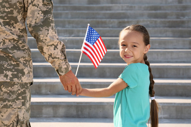 Soldier and his little daughter with American flag holding hands outdoors. Veterans Day in USA - Foto, Imagen