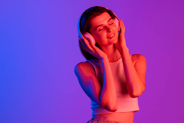 Half-length portrait of young girl isolated on purple, lilac color studio background in neon light. Concept of human emotions, facial expression, cosmetics, youth - Foto, imagen