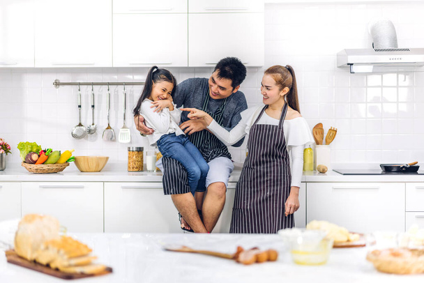 Portrait of enjoy happy love asian family father and mother with little asian girl daughter child having fun cooking food together with baking cookie and cake ingredient on table in kitchen - Photo, Image