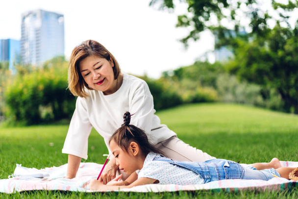 Portrait of happy love asian grandmother and little asian cute girl enjoy relax in summer park.Young girl with their laughing grandparents smiling together.Family and togetherness - Фото, изображение