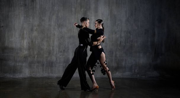 Siyah elbiseli genç dans salonu çifti stüdyo arka planında şehvetli bir şekilde dans ediyor. Latin dansı yapan profesyonel dansçılar. Balo dansı konsepti. İnsani duygular - aşk ve tutku - Fotoğraf, Görsel