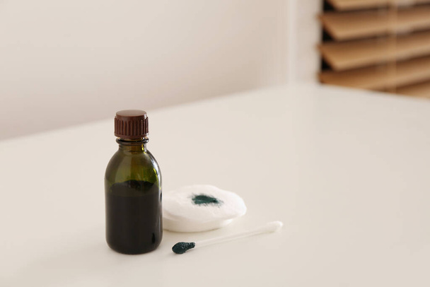 Bottle of brilliant green, cotton bud and pads on white table indoors - Photo, image