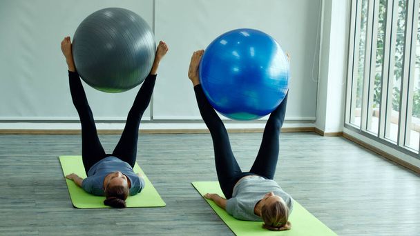 Beautiful two women doing yoga practice together. They lay down and playing with big ball tool. The concept for self-care sport and body balance. - Foto, Imagen