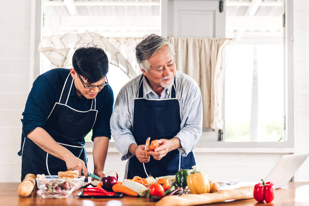 Portrait d'amour heureux famille asiatique père mature aîné et jeune fils adulte s'amuser à cuisiner ensemble et à la recherche d'une recette sur Internet avec ordinateur portable pour préparer le délicieux déjeuner - Photo, image