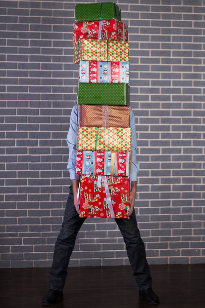 A man holds a stack of gift boxes in his hands. Many New Year gifts. - Foto, Bild