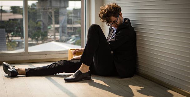 Close up of frustrated Caucasian businessman sitting on a floor with his knees up. Discouraged and hopeless expression. Financial problem, unemployment, bankruptcy concept. - Photo, Image