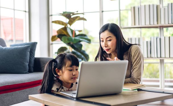 Matka i azjatyckie dziecko mała dziewczynka uczenia się i patrząc na laptopa podejmowania pracy domowej studiuje wiedzę z edukacji online e-learning system.children wideokonferencja z nauczycielem nauczycielem w domu - Zdjęcie, obraz
