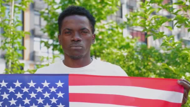 Zblízka afro-americký muž drží americkou vlajku a vypadá kamera - Záběry, video