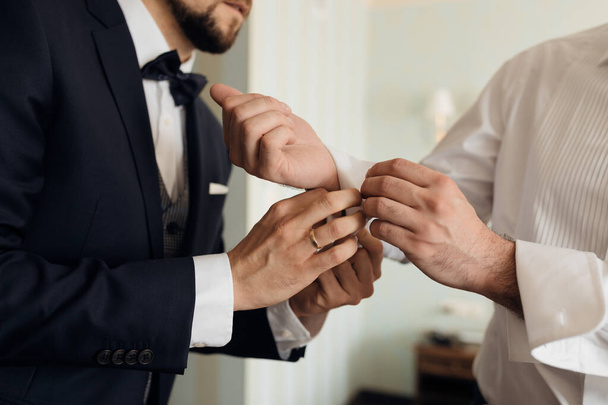 Witness at wedding fastens cufflinks in groom's shirt. Wedding gatherings and preparations for the celebration. Concept of happy life. High quality photo - Foto, Bild
