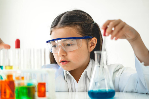 Cute little girl student child learning research and doing a chemical experiment while making analyzing and mixing liquid in glass at science class in school.Education and science concept - Foto, Bild