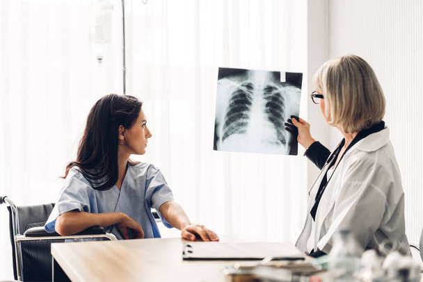 Médica idosa vestindo uniforme com serviço de estetoscópio ajuda a apoiar a discussão e olhar para a foto de filme de raio-x de tórax de paciente com pneumonias pulmonares. - Foto, Imagem