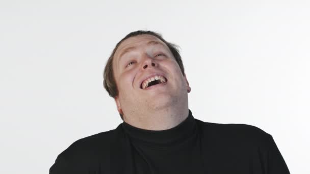 Mittlere Nahaufnahme Porträt mit langsamem, emotionalem jungen Mann, der vor weißem Hintergrund vor laufender Kamera lacht - Filmmaterial, Video