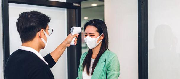 Группа профессионалов азиатского бизнеса и использование инфракрасного термометра для проверки температуры тела персонала лихорадка перед работой в карантине для коронавируса носить защитную маску в офисе - Фото, изображение