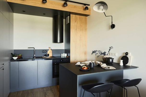 Stylish composition of modern small dining space interior. Black table, black and light wooden kitchen and dining accessories. Kitchen in the backgroud. Neutral walls. Minimalistic masculine concept. Details. Template. - Foto, afbeelding