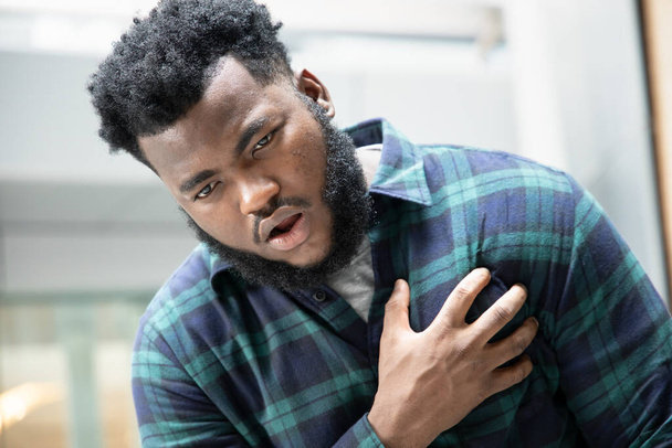 zieke Afrikaan met een hartaanval of pijn op de borst; portret van een Afrikaanse man die lijdt aan een hartaanval, pijn op de borst, gezondheidsconcept; jonge volwassen Afrikaan of zwarte man model - Foto, afbeelding