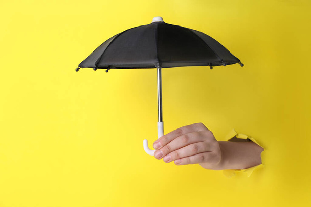Woman holding open small black umbrella through hole in yellow paper, closeup - Φωτογραφία, εικόνα
