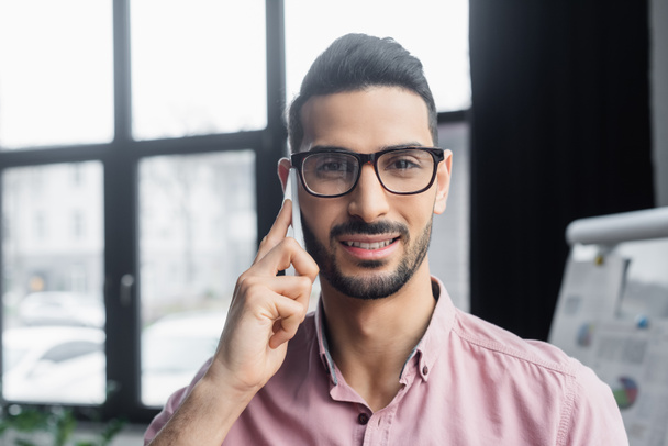 Fiatal arab üzletember szemüvegben mosolyog, miközben mobilon beszél.  - Fotó, kép