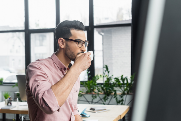 Αραβας επιχειρηματίας με γυαλιά ηλίου πίνοντας καφέ στο γραφείο  - Φωτογραφία, εικόνα