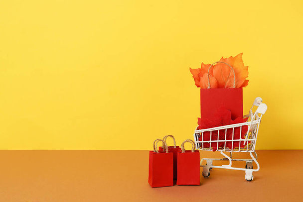 黄色の背景に紙袋と赤い落下葉を持つ秋の買い物食料品のカート。コンセプト秋の販売。コピースペース - 写真・画像