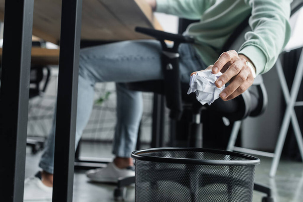 Περικοπή άποψη του θολή επιχειρηματίας κρατώντας τσαλακωμένο χαρτί κοντά σε σκουπιδοτενεκέ στο γραφείο  - Φωτογραφία, εικόνα
