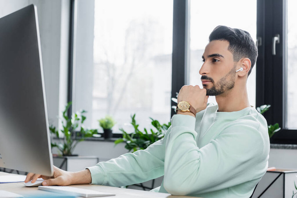 Arabe homme d'affaires en écouteur sans fil en utilisant l'ordinateur dans le bureau  - Photo, image
