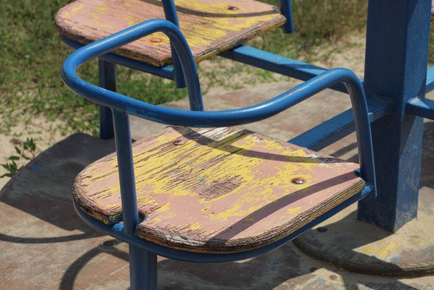 one empty colored wooden seat on a child blue metal carousel wheel in the playground in the park - Photo, Image