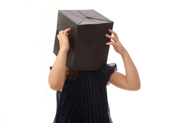 Portrait isolé d'une jolie fille qui s'amuse, mettant un paquet de courses noires sur sa tête, posant sur fond blanc, copiant de l'espace. Concept Black Friday - Photo, image