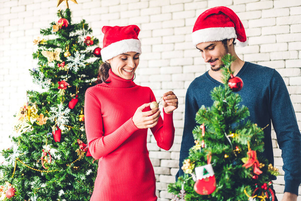 Noel Baba şapkalı romantik çift Noel ağacını süsleyerek ve gülerek Noel arifesini kutlarken ve Noel zamanı evde birlikte vakit geçirirken eğleniyor. - Fotoğraf, Görsel