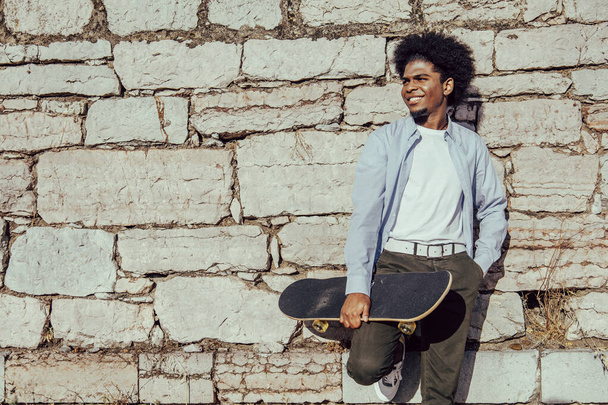 Young African American student leaning against a wall with skateboard. Copy space - Foto, immagini