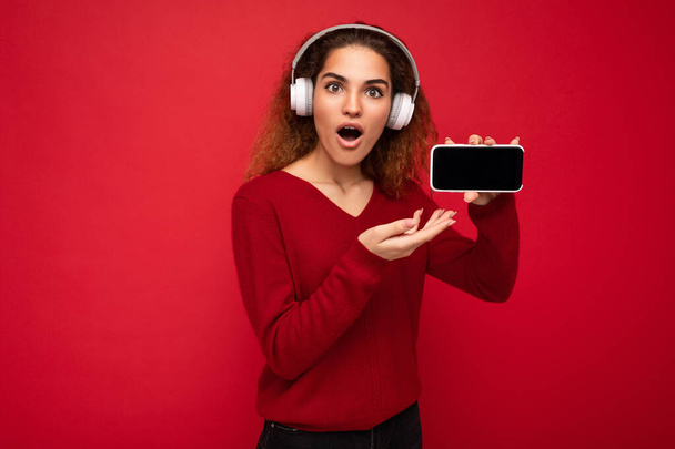 Приваблива позитивна шокована здивована молода жінка в стильному повсякденному вбранні ізольована на барвистій стіні, що тримає і показує мобільний телефон з порожнім екраном для вирізання в білому Bluetooth
 - Фото, зображення