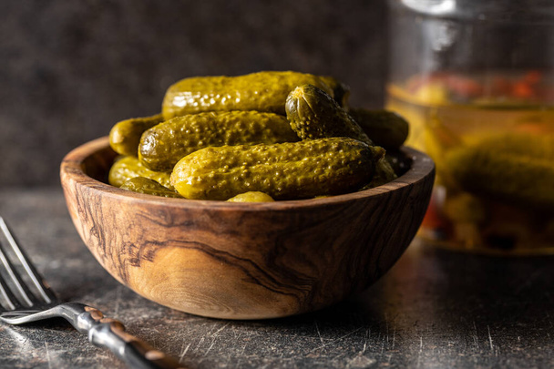 Small pickles. Marinated pickled cucumbers in wooden bowl on black table. - Foto, imagen