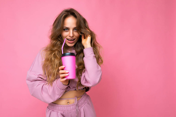 Photo of sexy attractive young happy smiling blond woman wearing everyday stylish clothes isolated over colourful background wall holding paper cup for cutout drinking tea looking at camera - Foto, Imagen
