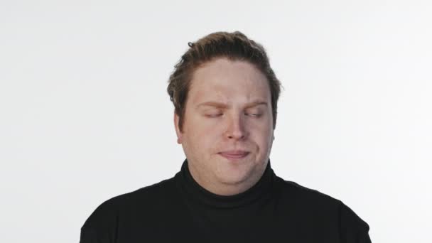 Medium close-up portrait of young man with poker face looking at camera indifferently standing at white background - Footage, Video