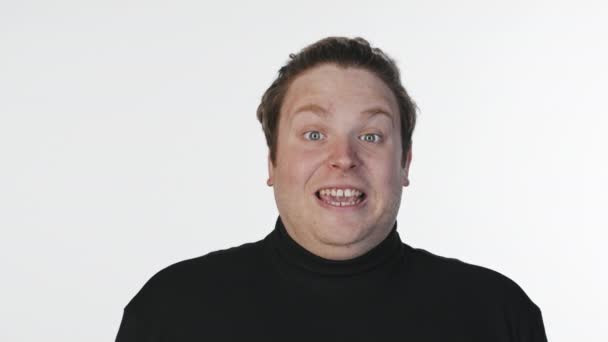 Medium close-up portret met slow mo van opgewonden jonge blanke man gezichten trekken op camera staan op witte achtergrond in de studio - Video