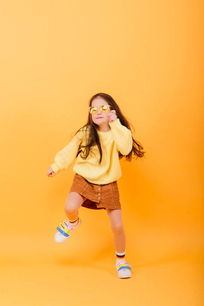 Close-up portrait of cute little girl. Studio shot over yellow background. Childhood concept. - Photo, Image