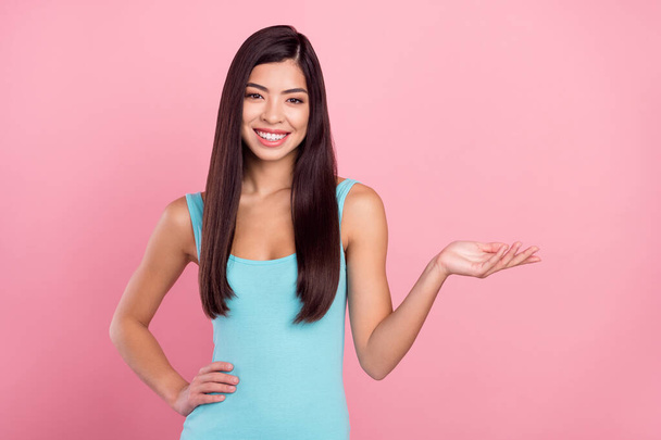 Photo portrait woman wearing blue dress smiling demonstrating copyspace palm isolated pastel pink color background - 写真・画像