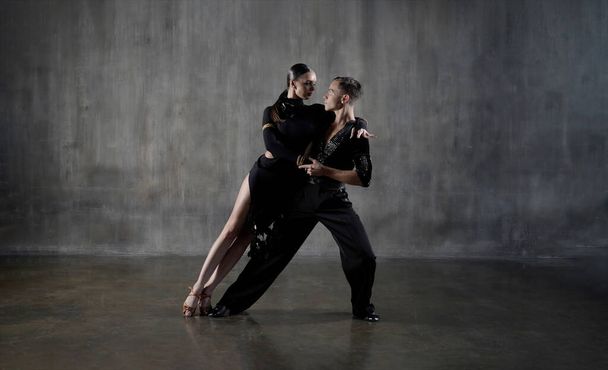 The young millennial dance ballroom couple in black dress dancing in sensual pose on studio background. Professional dancers dancing latino. Hobby dance concept. Human emotions - love and passion - Φωτογραφία, εικόνα