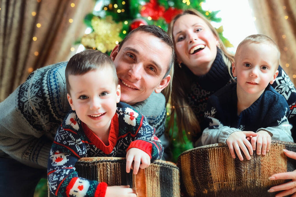 Молодая счастливая семья с двумя детьми празднует Рождество. Портрет веселой кавказской семьи из 4 человек  - Фото, изображение