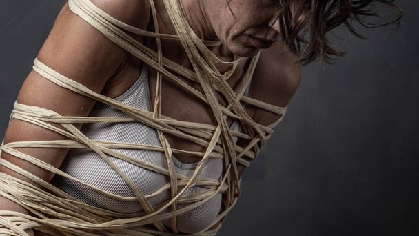 Portrait of a woman wrapped with a rope  over grey wall - Fotografie, Obrázek