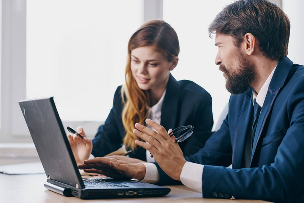 zakenman en -vrouw zitten achter een bureau met een laptop communicatietechnologie - Foto, afbeelding