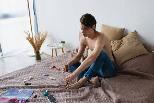 transgender young man in jeans holding nail polish in bedroom  - Фото, зображення