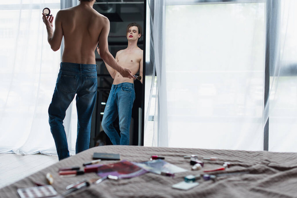 jeune homme transgenre tenant brosse cosmétique et poudre visage près du miroir  - Photo, image