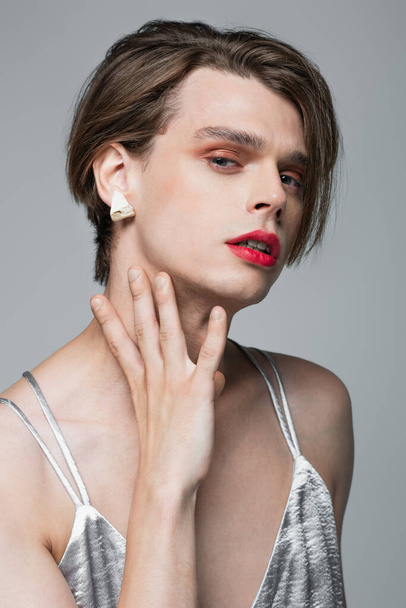 young transgender man with makeup and earring posing isolated on grey - Fotó, kép