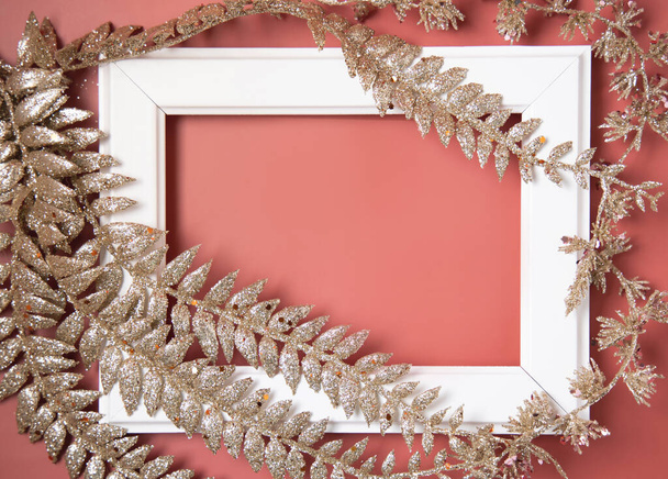 Weißer Rahmen bedeckt und dekoriert mit goldenen Weihnachtsblättern auf rosa Hintergrund von oben - Foto, Bild