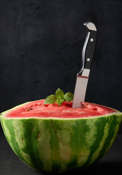 reife rote Wassermelone, die in einem großen Messer steckt. Schwarzer Hintergrund - Foto, Bild