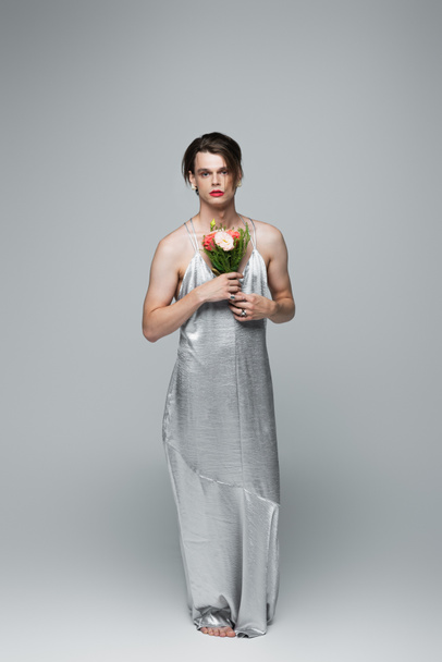 Transgender-Mann im Slip-Kleid posiert mit Blumen auf grau - Foto, Bild