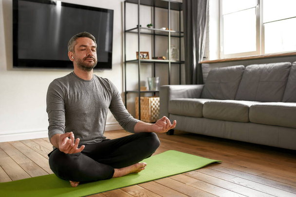 Ruhige Männer mit Kopfhörern meditieren zu Hause Yoga - Foto, Bild